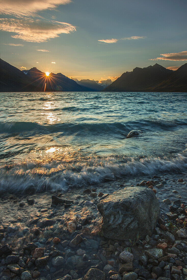 The sun rises as soft waves brush the shoreline of upper Twin Lake in Lake Clark National Park & Preserve, Alaska.