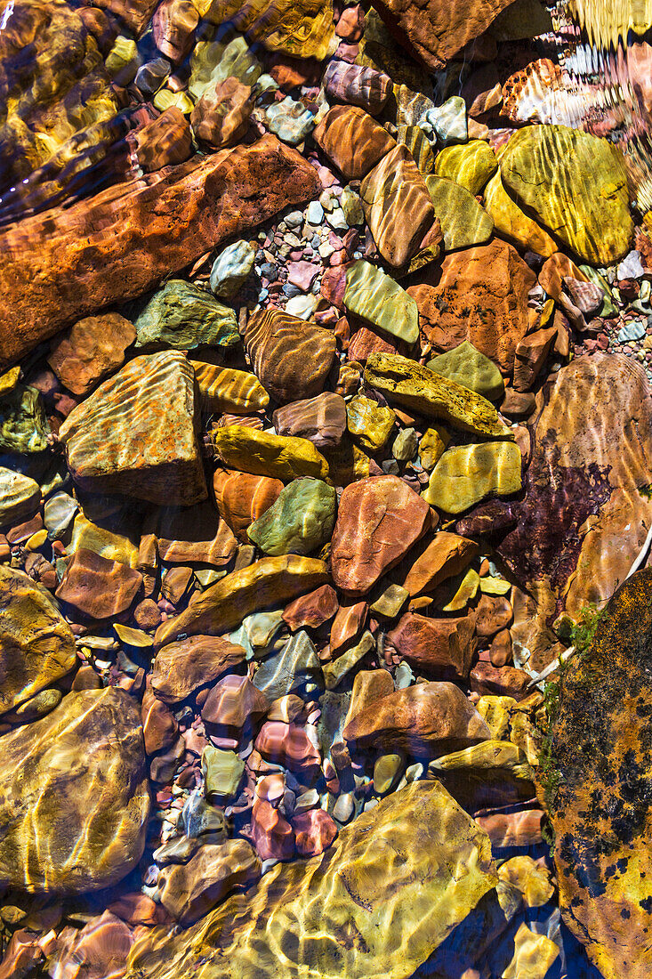 'Close up of colourful creek stones underwater with ripples in water; Waterton, Alberta, Canada'