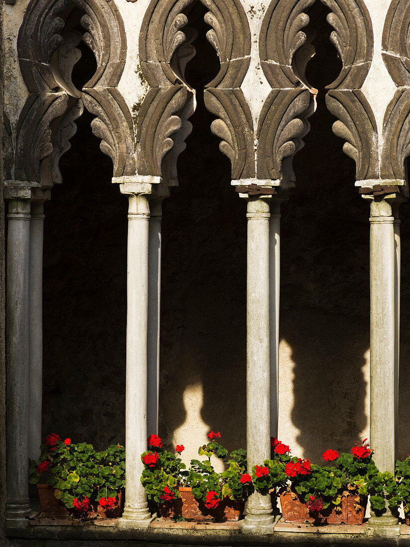 'Decorative pillars and a facade of a building with red flowers lining a ledge; Amalfi, Campania, Italy'