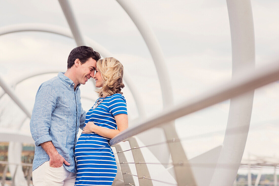 Smiling Caucasian man and expectant mother rubbing noses on walkway