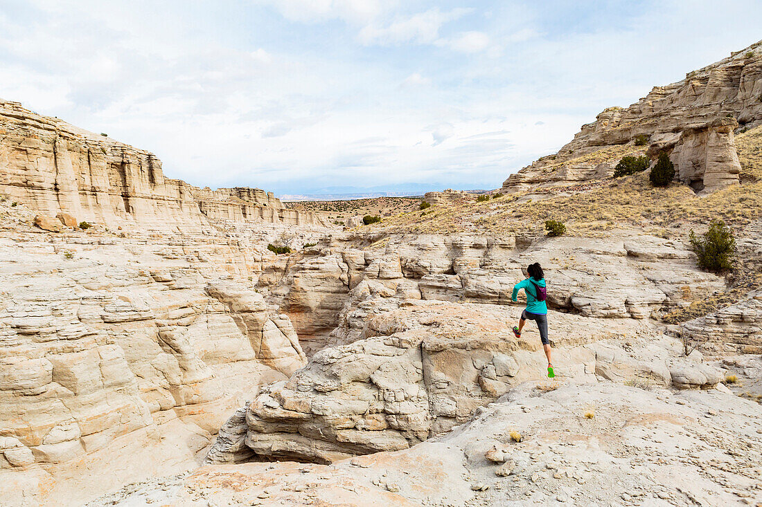 Women jumping to rock in canyon wearing backpack