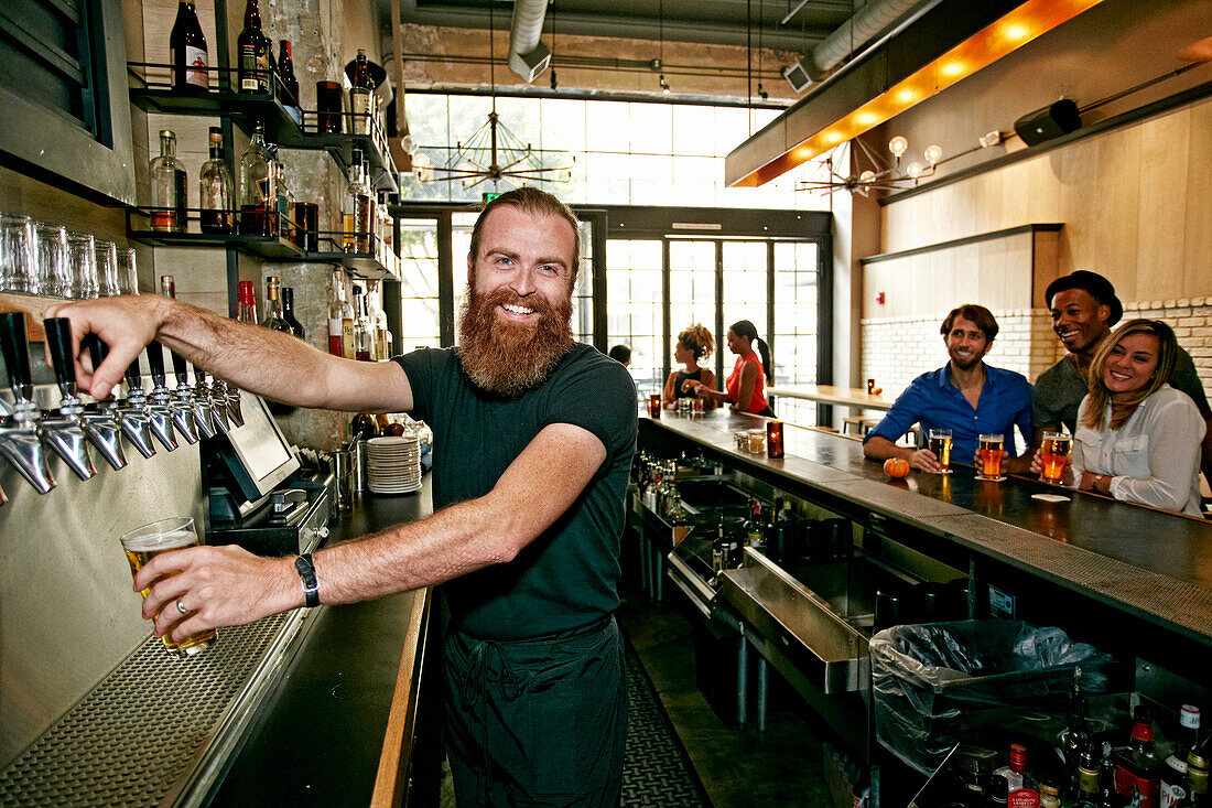 Smiling bartender pouring beer at bar