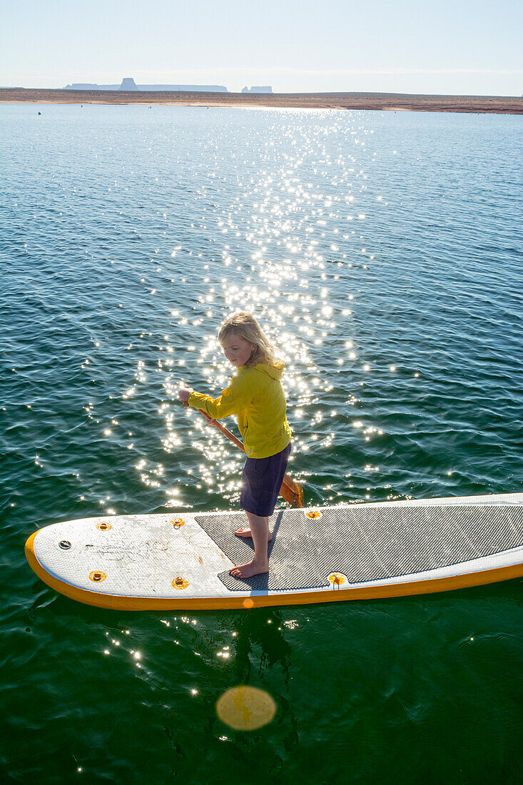 A young girl paddleboarding on Lake Powell, Wahweap Marina, Glen Caynon National Recreation Area, Page,  Arizona.