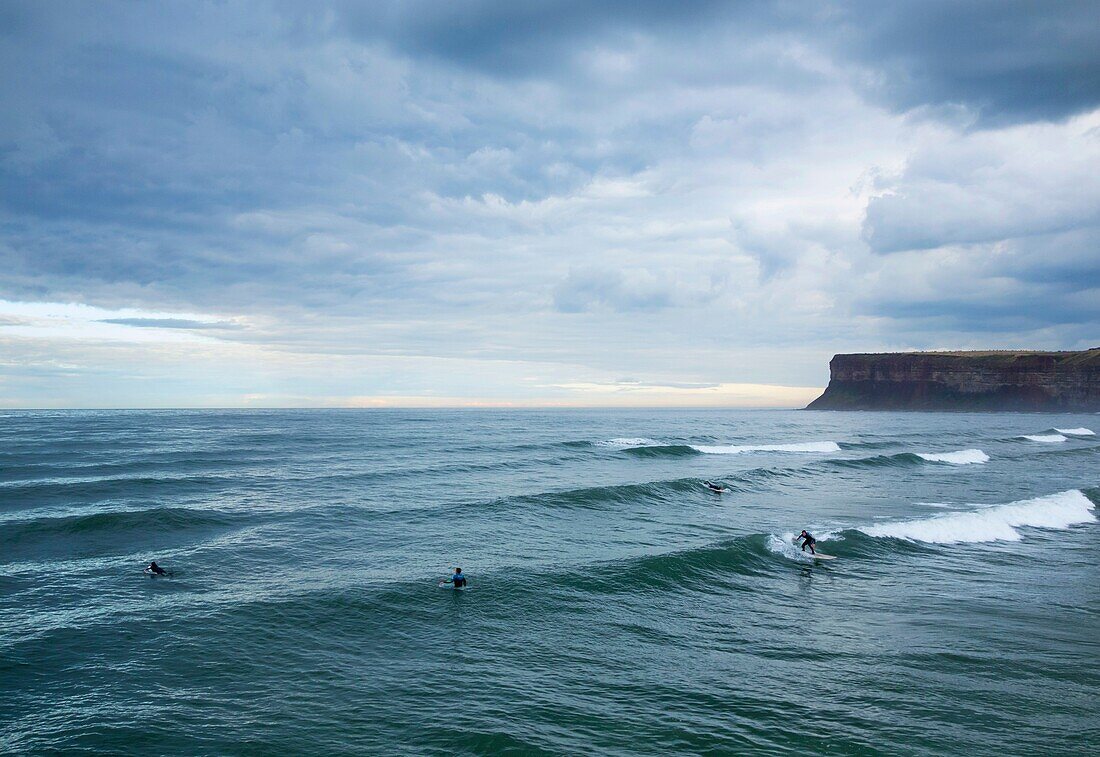 Saltburn by the Sea, North Yorkshire, England, United Kingdom. Europe. Surfers under a stormy sky at Saltburn on the North Yorkshire coast.