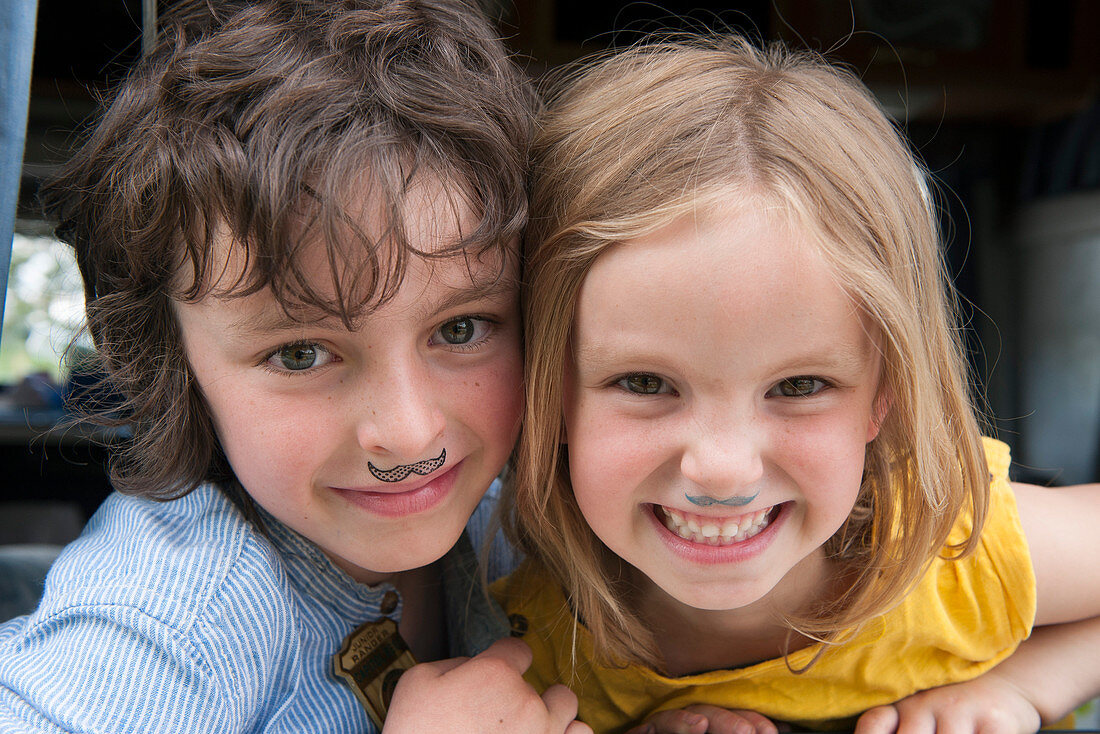 Young siblings wearing fake mustaches, portrait