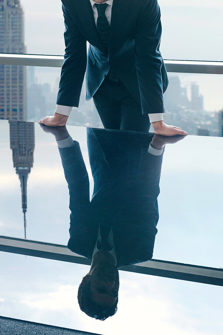 Businessman leaning against table, reflection in glass top