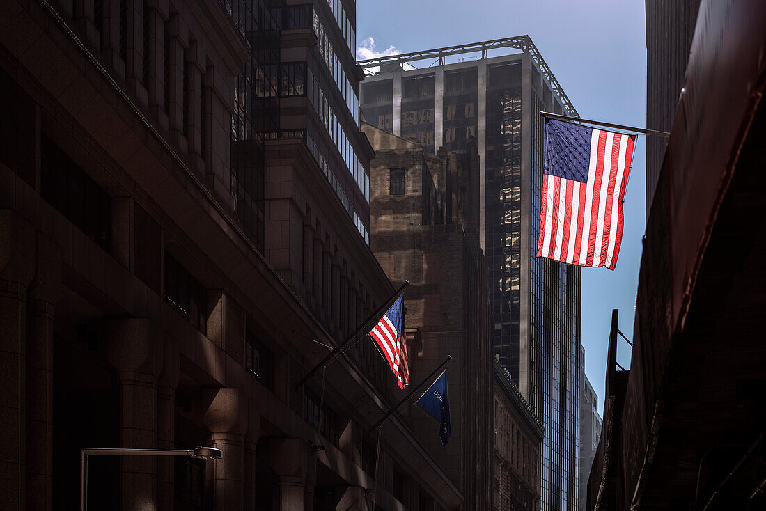 amerikanische Flaggen im Gegenlicht zwischen den Häuserschluchten nahe der Wall Street, Manhattan, New York, USA, Vereinigte Staaten von Amerika