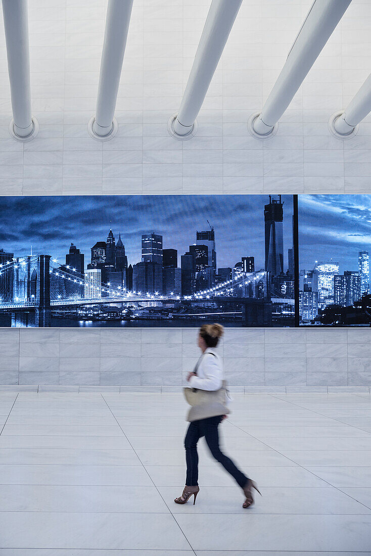 Frau läuft an Leuchtreklame in einem Korridor von the Oculus vorbei und sieht dabei die Skyline von New York, futuristischer Bahnhof des Star Architekten Santiago Calatrava bei der World Trade Center Gedenkstätte, Manhattan, New York, USA, Vereinigte Staa