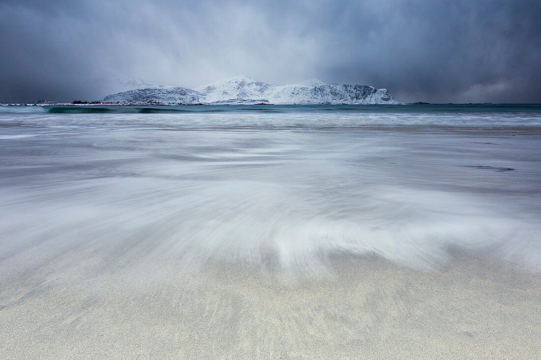 Waves of the icy sea on the beach in the background the snowy peaks Ramberg Lofoten Islands Norway Europe