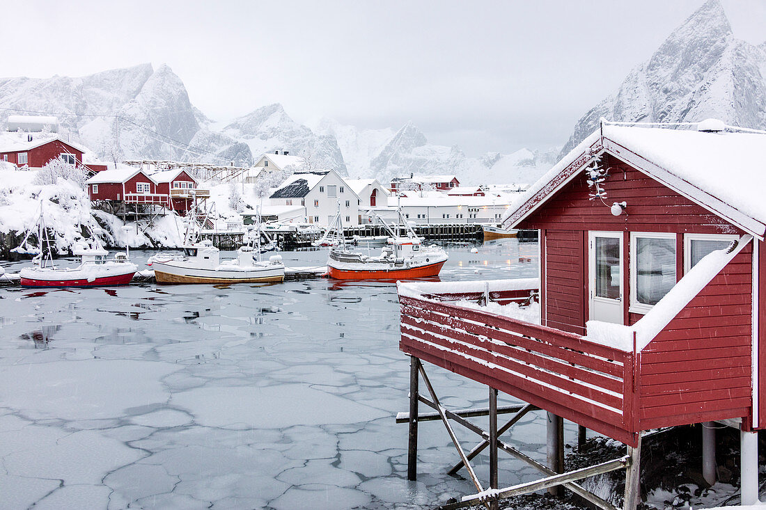 Icy sea and snowy peaks around the typical houses called rorbu and fishing boats Hamn?©y Lofoten Islands Northern Norway Europe