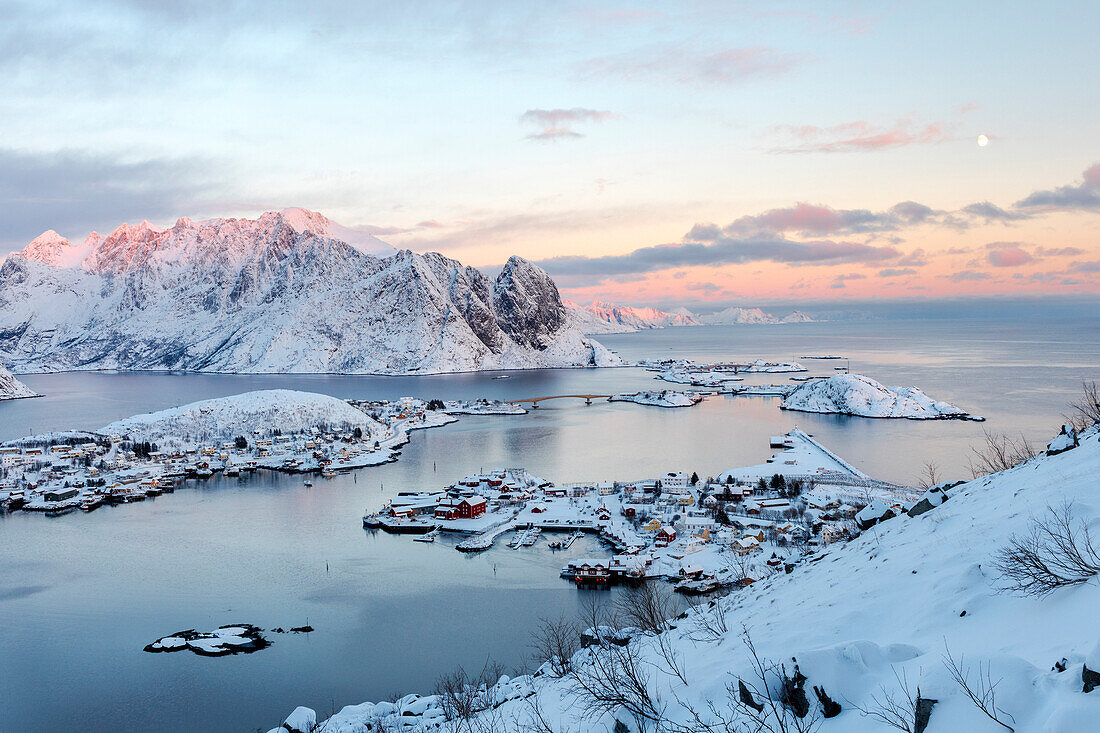 The pink colors of sunset and snowy peaks surround the fishing villages Reine Nordland Lofoten Islands Norway Europe