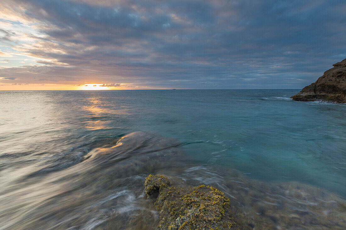 The lights of sunset are reflected in the blue sea Hawksbill Bay Caribbean Antigua and Barbuda Leeward Islands West Indies