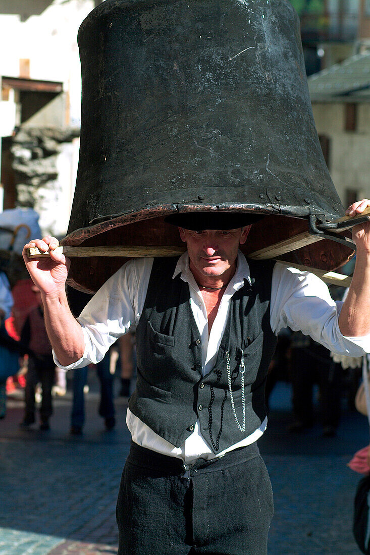 'A man wearing traditional clothes( in the style of the group ''I Giaroi'' from Valgerola) walks with a big pot trough the streets in Valgerola. This kind of pot is used by shepherds to cook milk during the process of making cheese. Valtellina Lombardy It