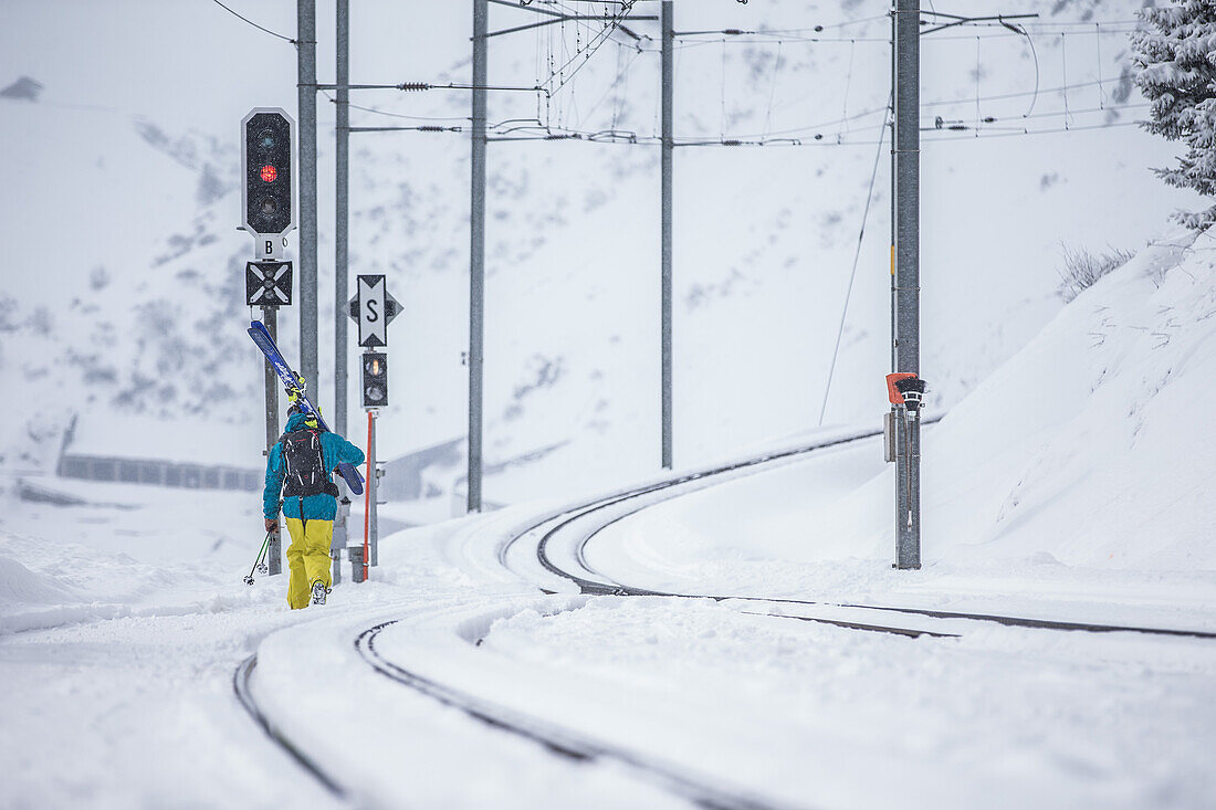 Junger Skifahrer lauft eine verschneite Eisenbahnschiene entlang, Andermatt, Uri, Schweiz