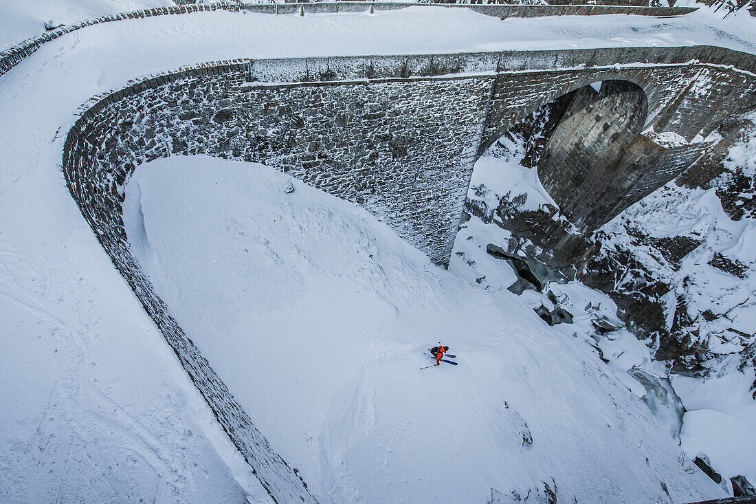 Junger Skifahrer fährt einen Abhang herunter neben einer Steinbrücke, Andermatt, Uri, Schweiz