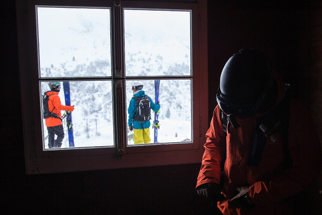 Junger Skifahrer breitet sich in einer Hütte vor während die anderen draußen warten, Andermatt, Uri, Schweiz