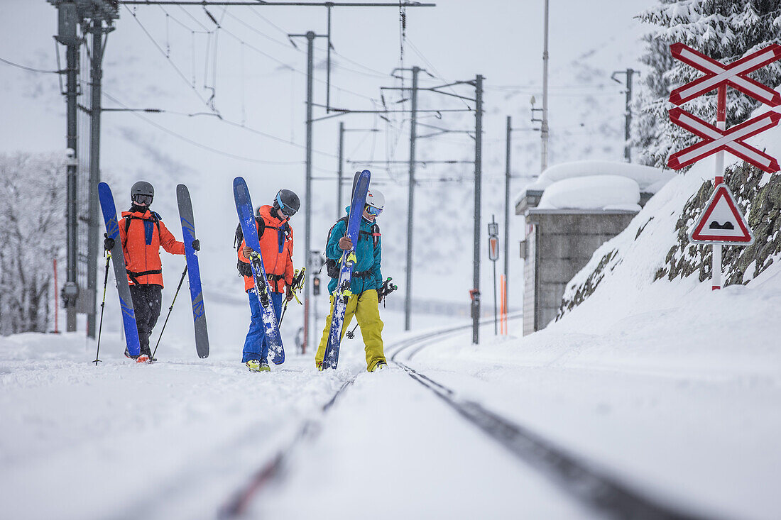 Drei junge Skifahrer gehen über Eisenbahnschienen, Andermatt, Uri, Schweiz