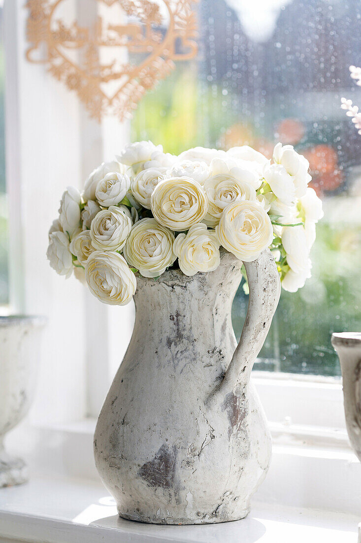 Imitation white roses in jug at window. England UK.