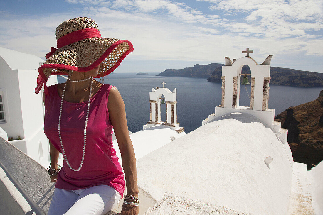 Frau vor einem Glockenturm in der Stadt Oia mit Blick auf die Caldera, Santorin, Kykladen, Griechische Inseln, Griechenland, Europa.