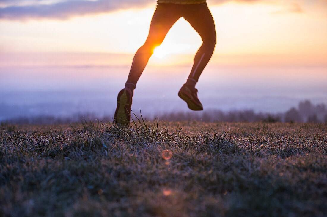 Junger Mann läuft über eine Wiese bei Sonnenaufgang, Allgäu, Bayern, Deutschland