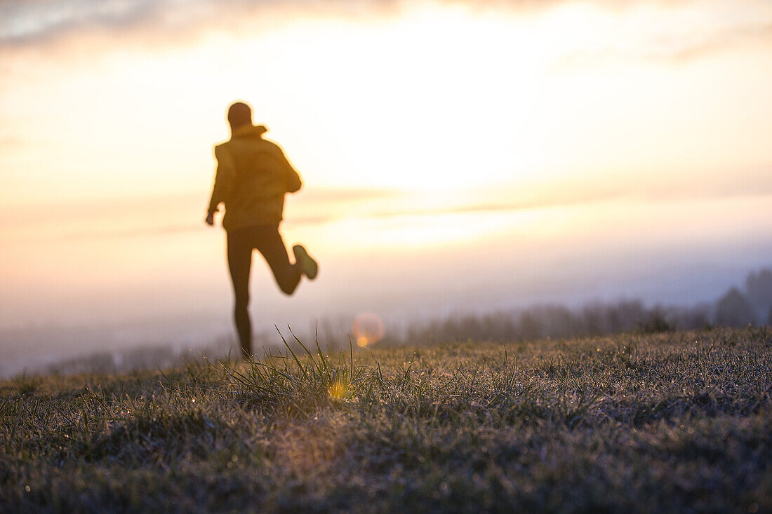 Junger Mann läuft über eine Wiese bei Sonnenaufgang, Allgäu, Bayern, Deutschland