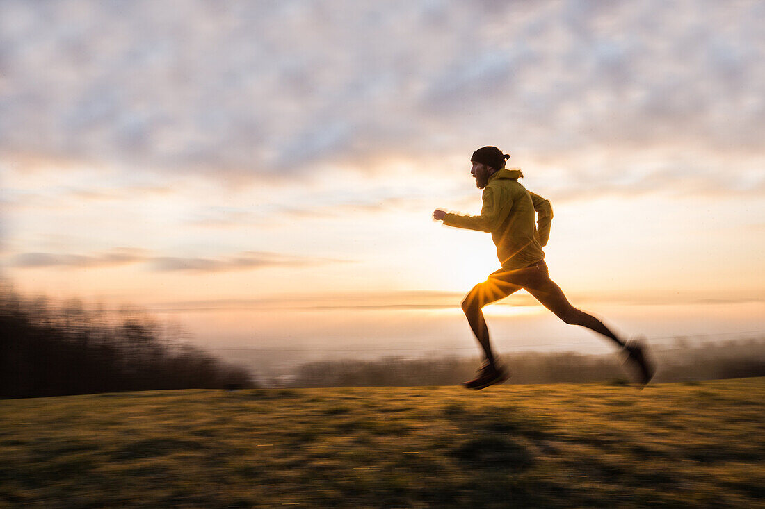 Young man running over a meadow during sunrise, Allgaeu, Bavaria, Germany