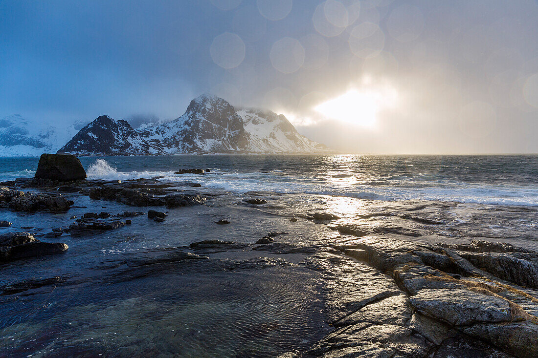 Sonne bricht durch die Wolken an der Felsküste bei Vareid, Flakstadoya, Lofoten, Norwegen, Skandinavien, Europa