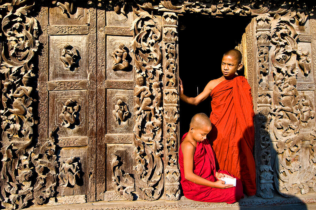 Myanmar (Burma), Mandalay Division, Mandalay, Shwe Nan Daw temple, monks A Shin Pyan ya Zaw Ta (15 years old) and A Shin Tay Zaw Barta (14 years old) reading in front of the carved panels made of teak