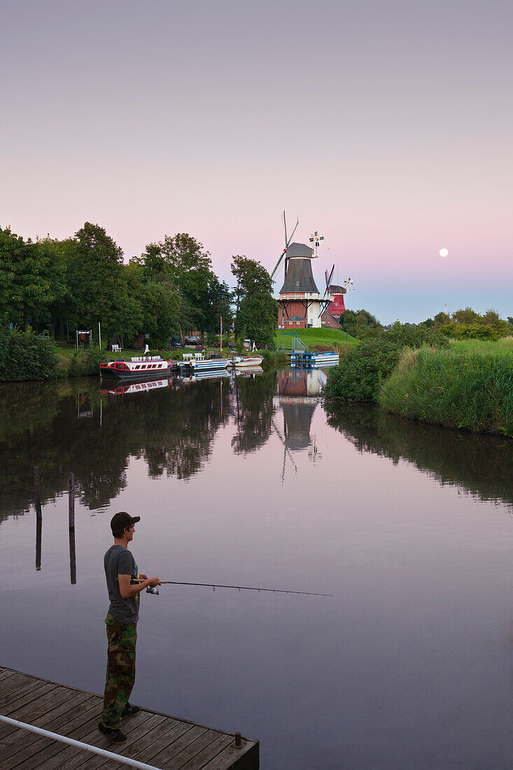 Angler at the twin windmills, at full moon, Greetsiel, East Friesland, Lower Saxony, Germany