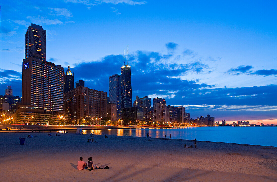 United States, Illinois, Chicago, Gold Coast and buildings at the edge of Michigan Lake at sunset seen from Olive Park, couple sitting on the sand