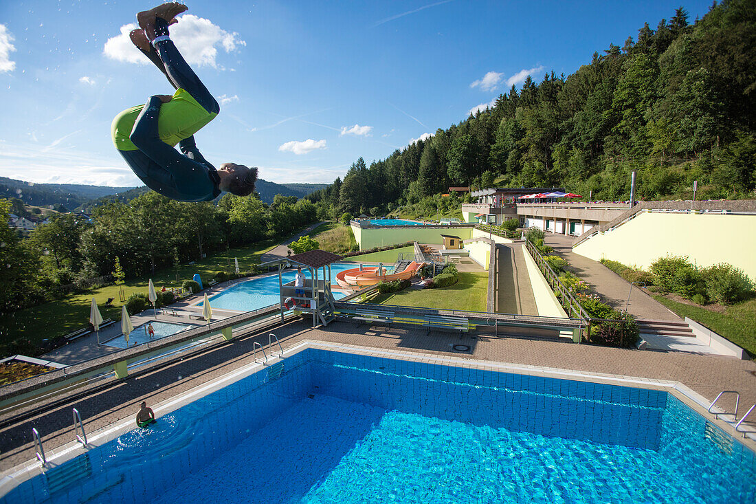 Young man jumps from 5 meter diving tower into swimming pool at Freibad Terrassenbad Frammersbach, Frammersbach, Spessart-Mainland, Bavaria, Germany