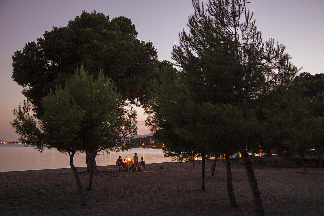 People enjoy dinner at picnic table near beach at dusk, near Port d'Alcudia, Mallorca, Balearic Islands, Spain