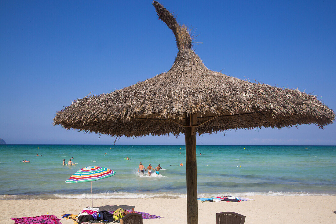 Thatched beach umbrella and people in water at Playa de Muro beach, near Can Picafort, Mallorca, Balearic Islands, Spain