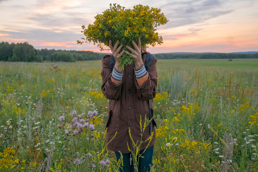 Caucasian woman holding bouquet of flowers over face in field at sunset