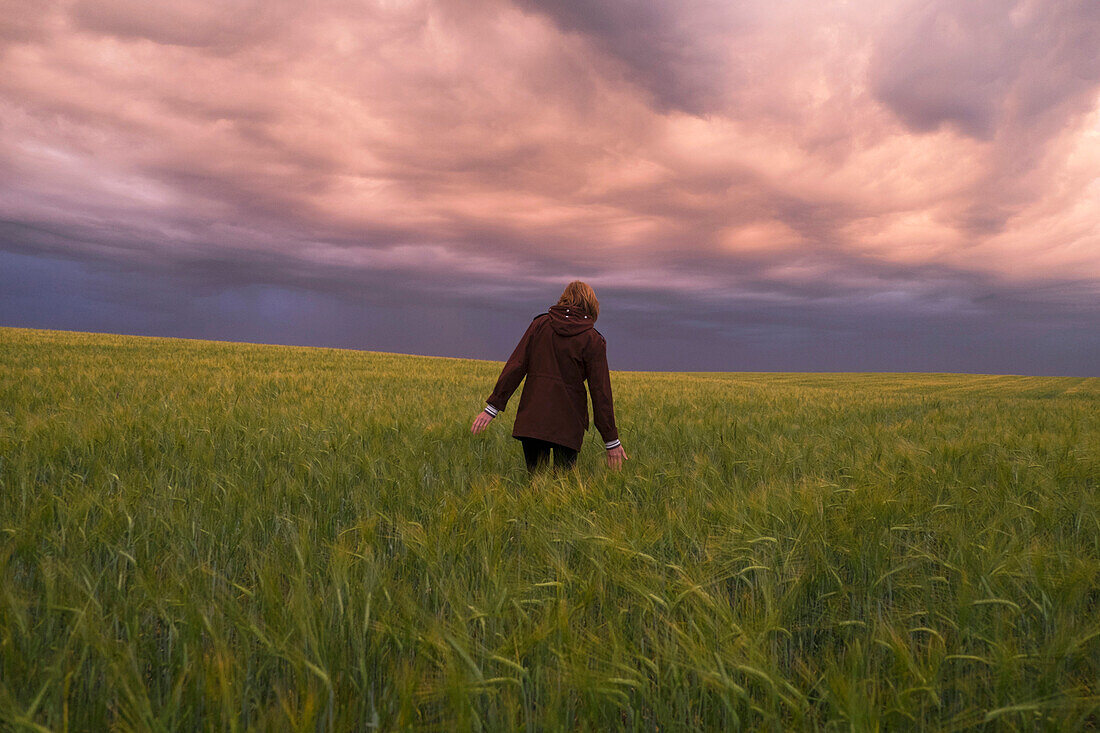 Storm clouds over Caucasian woman walking in field of tall grass