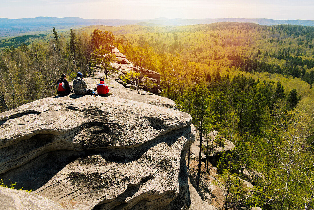 Caucasian friends sitting on mountain rock admiring scenic view