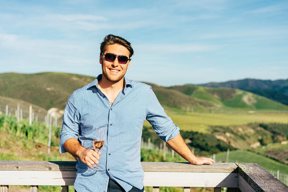 Caucasian man leaning on balcony drinking wine