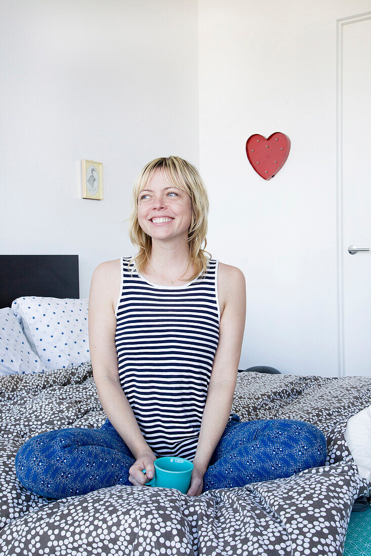 Caucasian woman sitting on bed drinking coffee