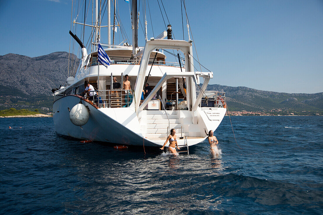 Zwei junge Frauen springen ins Wasser von der Deck Plattform von Motorsegler Kreuzfahrtschiff M/S Panorama (Variety Cruises) auf Reede während eines Badeaufenthalts für die Passagiere, nahe Korcula, Dubrovnik-Neretva, Kroatien