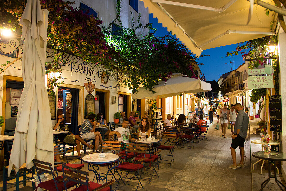 Menschen sitzen draußen vor einer Bar bzw. einem Café in der Altstadt und genießen Drinks in der Abenddämmerung, Gaios, Paxos, Ionische Inseln, Griechenland