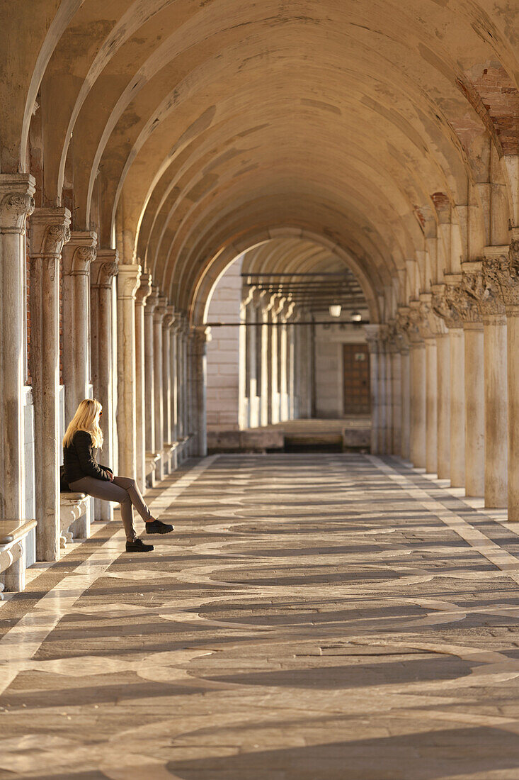 Woman sitting under the collonade of the Doge's Palace, Venice, Italy