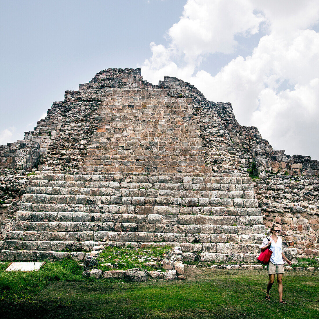 A young woman in a white shirt and tan shorts walks near a Mayan stone pyramid ruin near Merida, Mexico.