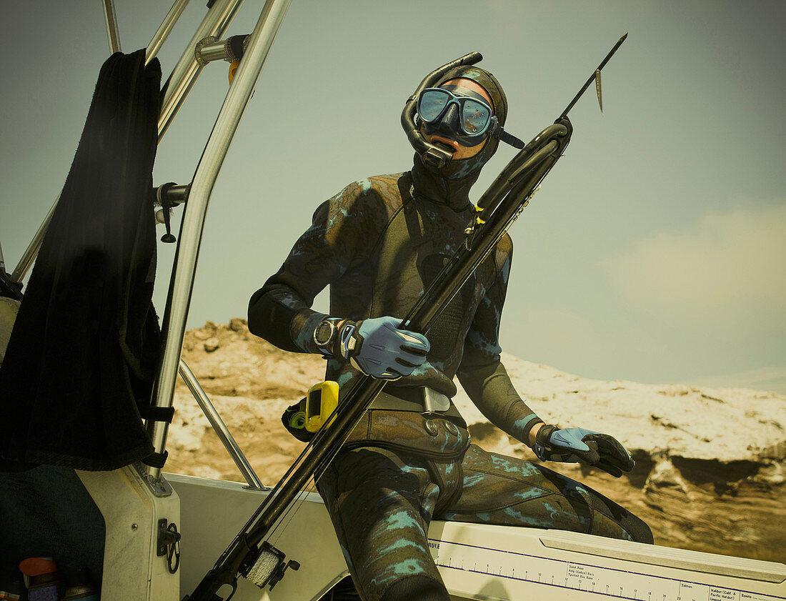 A spear fisher ready to dives with his spear gun, sits on his boat.