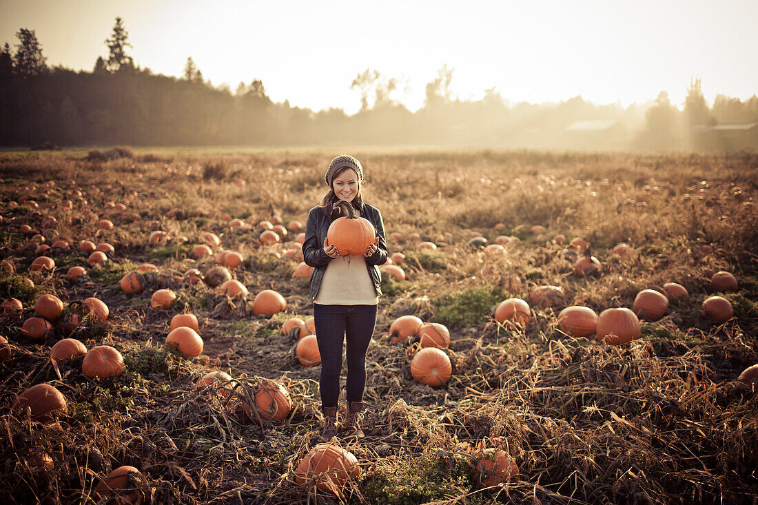 A young woman holds a pumkin while at the pumpkin patch.