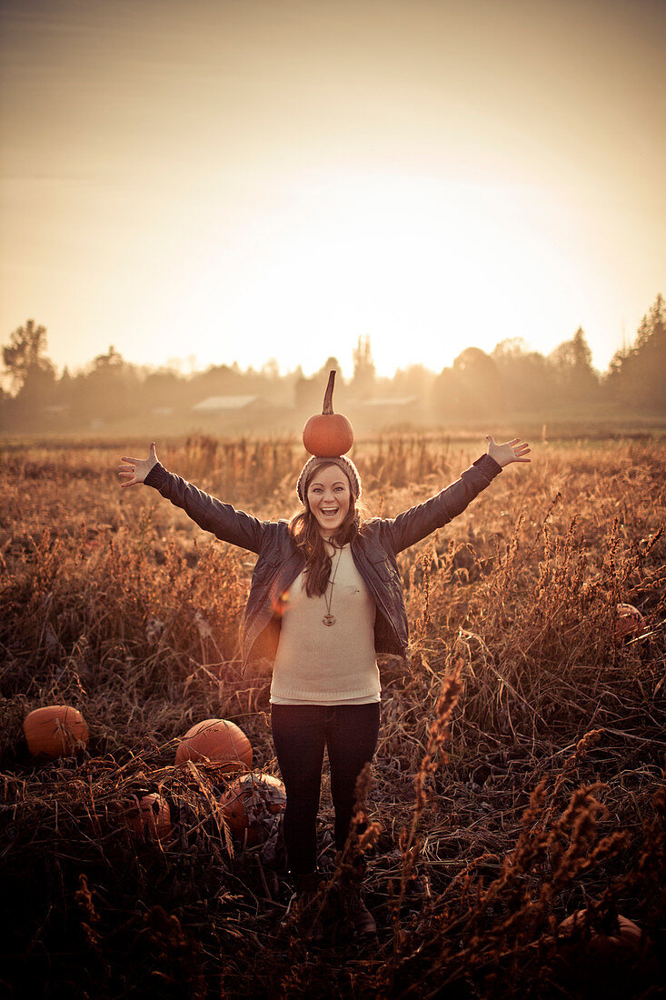A young woman balances a pumpkin on her head.