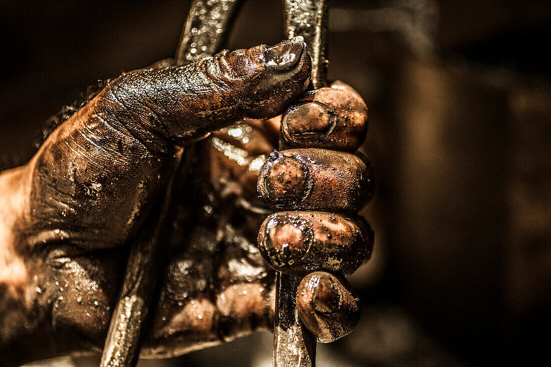 Man's hand covered with grease and oil while holding on to a tool.