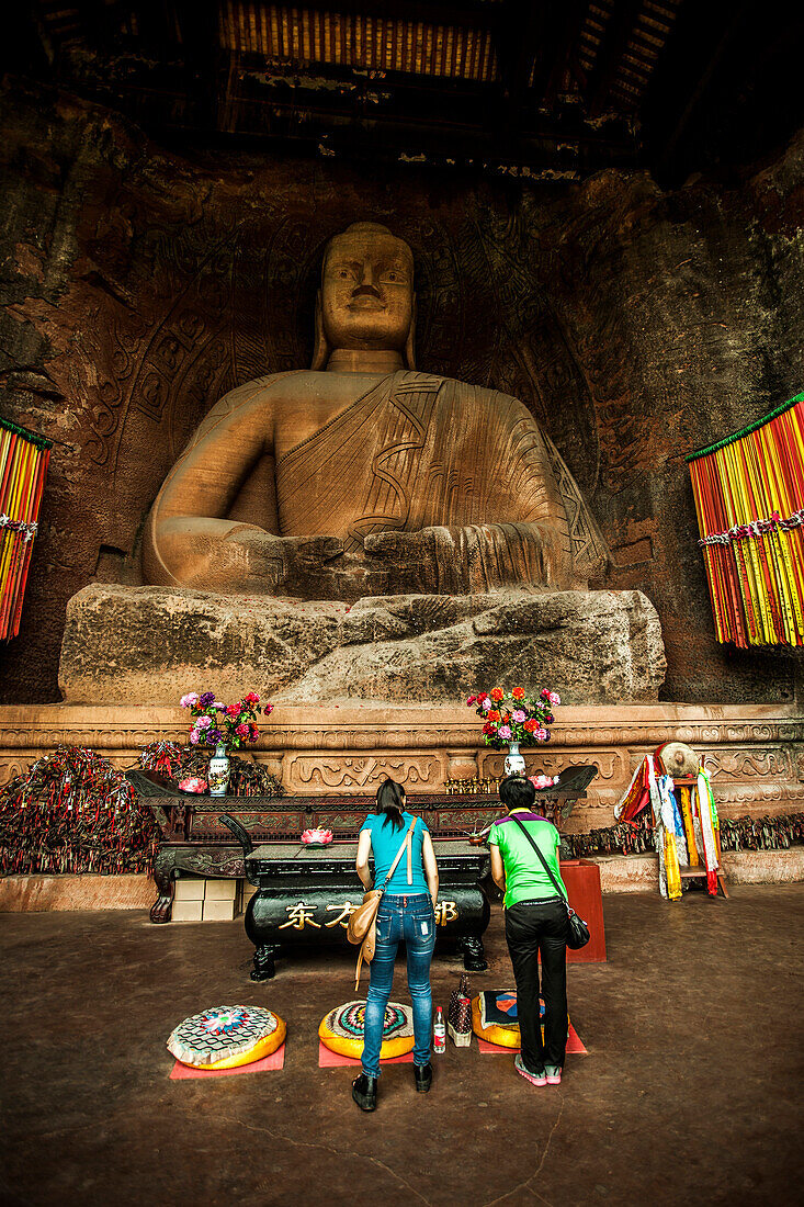 Chinese women praying in front of a carved stone Buddha in Leshan, China.