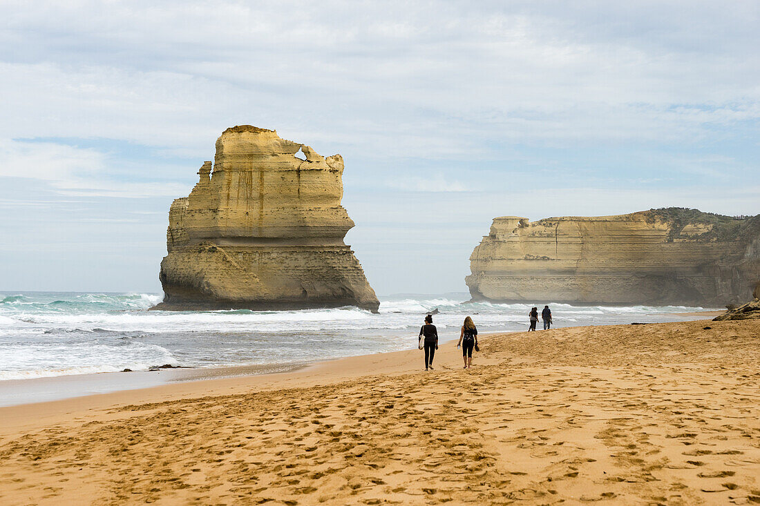 People walk along a beach with one of the Twelve Apostles geological formation in the background, Victoria, Australia, Pacific