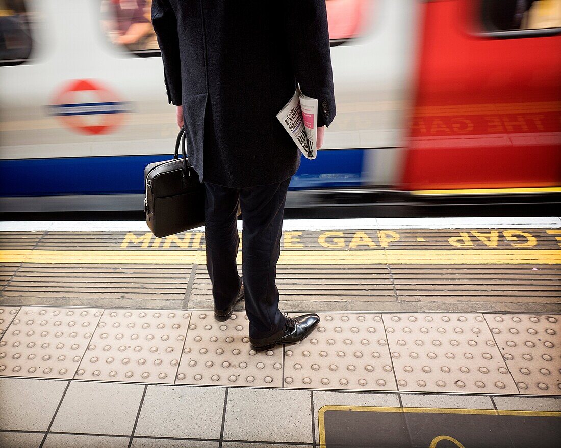 Un Hombre ejecutivo con un porta documentos y un periodico en las manos esperando en el anden del anderground de London y un tren en movimiento Bank Station, London, Reino Unido, Europa