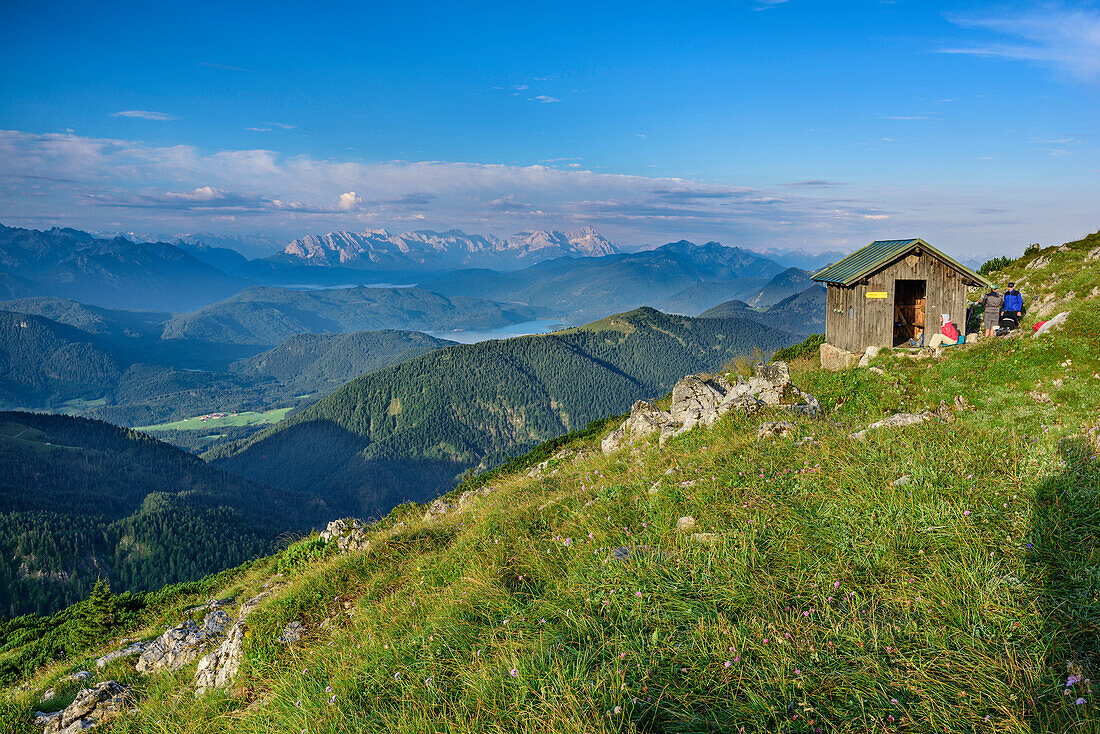 Several persons standing at hut at Benediktenwand, Wetterstein range in background, from Benediktenwand, Bavarian Alps, Upper Bavaria, Bavaria, Germany